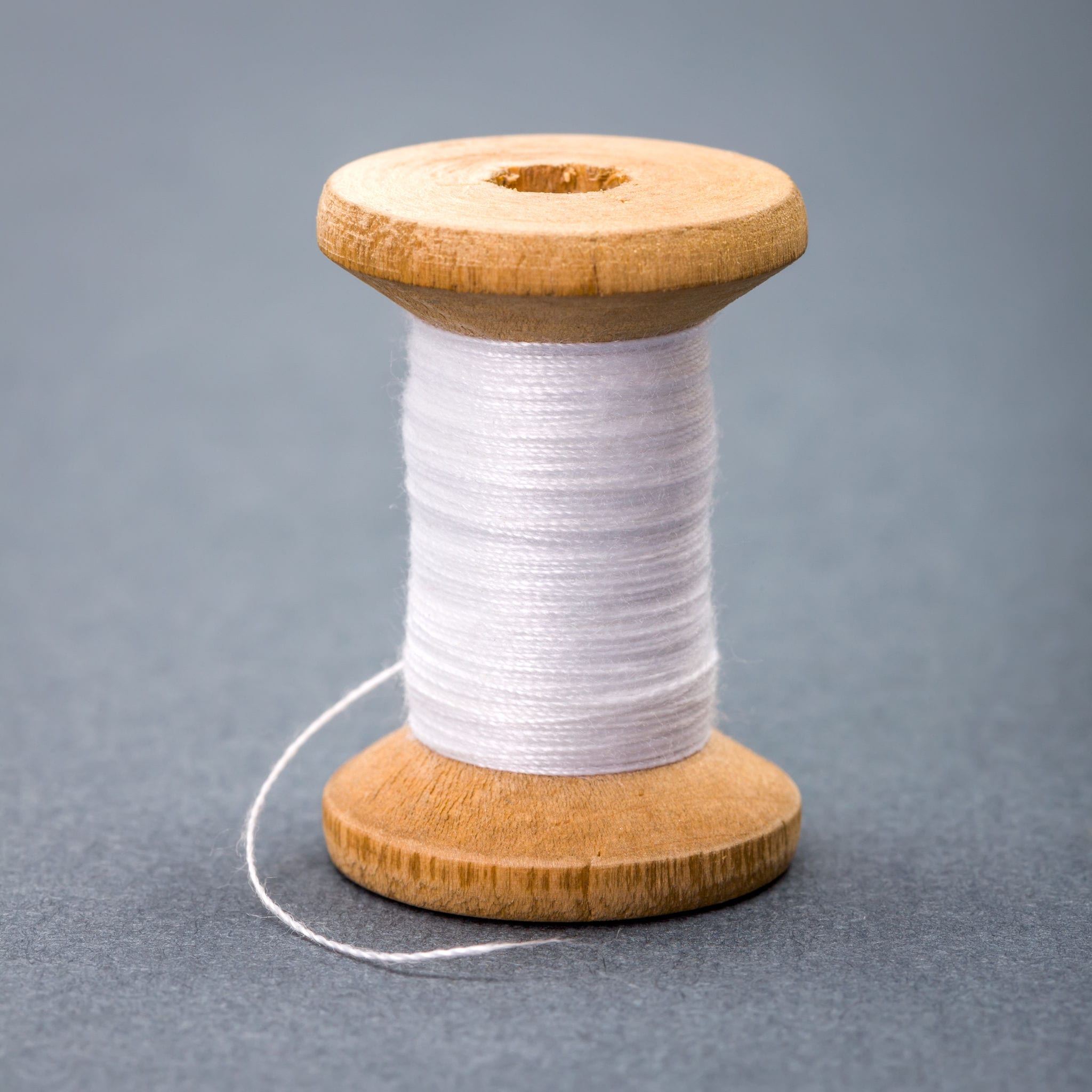 Vintage wooden spool of white sewing thread on gray background